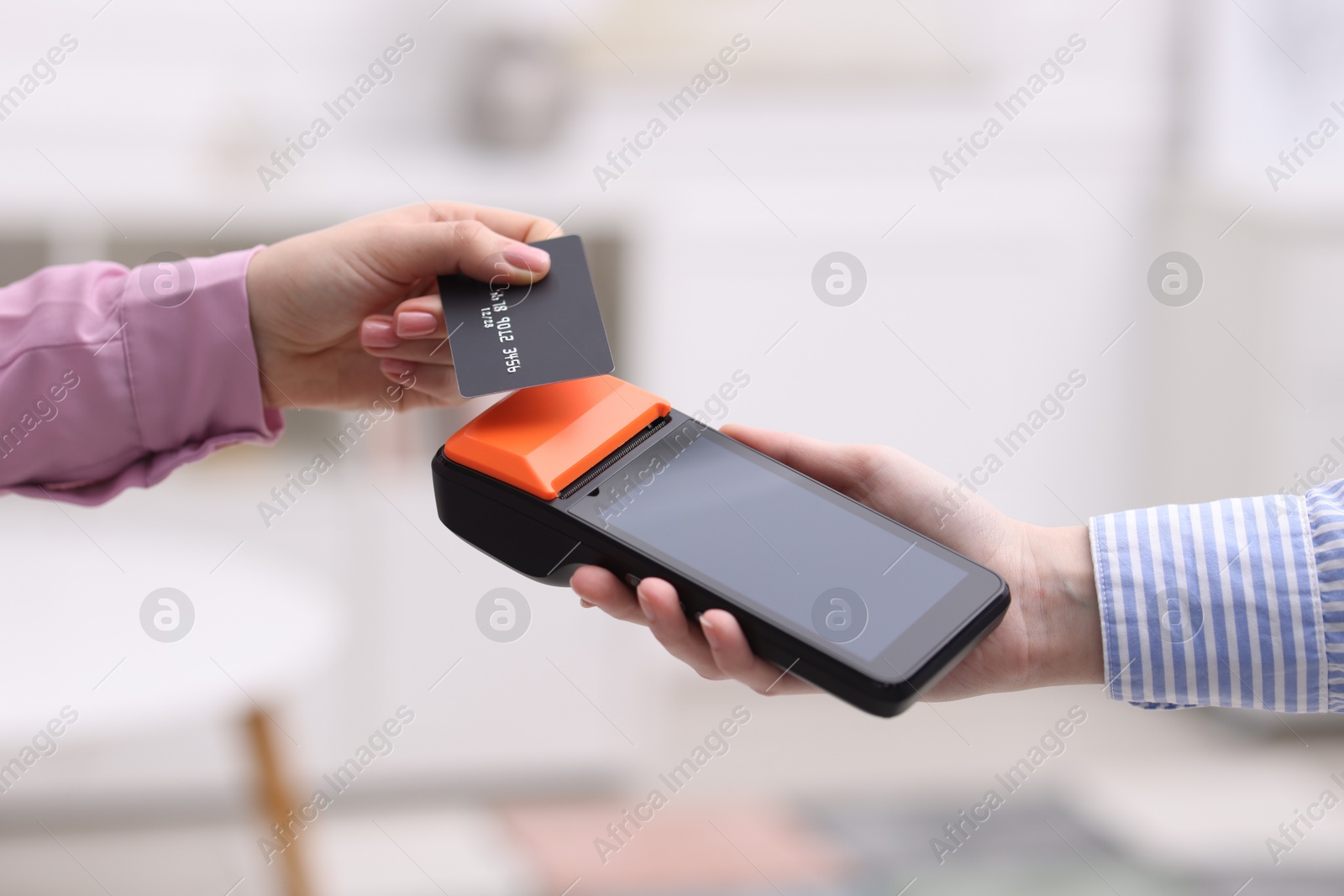 Photo of Woman paying with credit card via terminal against blurred background, closeup