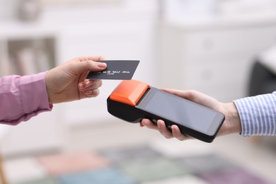 Photo of Woman paying with credit card via terminal against blurred background, closeup