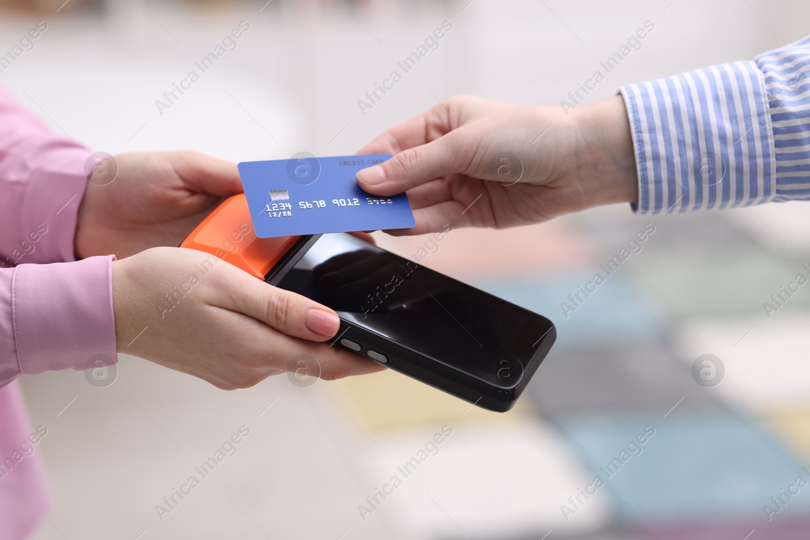 Photo of Woman paying with credit card via terminal against blurred background, closeup