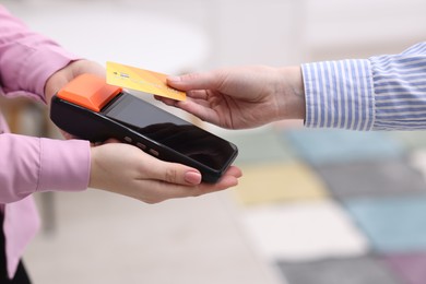 Woman paying with credit card via terminal against blurred background, closeup