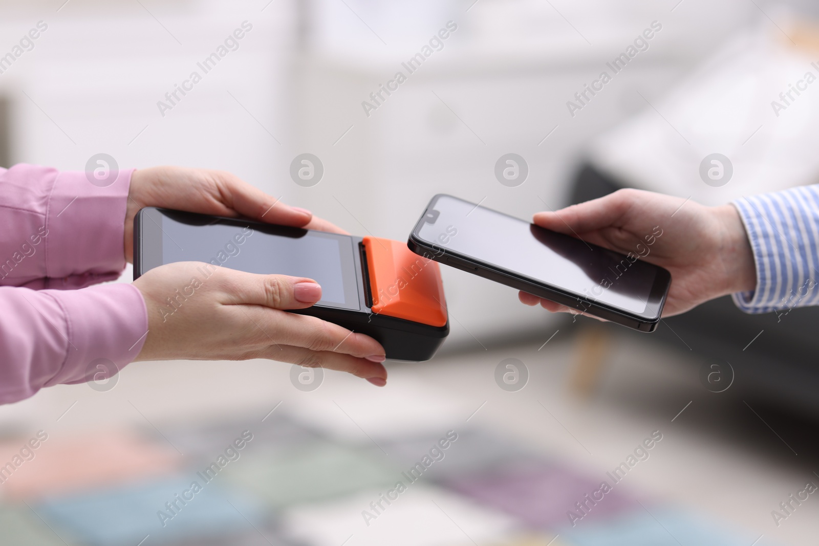 Photo of Woman paying with smartphone via terminal against blurred background, closeup