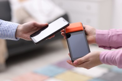 Photo of Woman paying with smartphone via terminal against blurred background, closeup