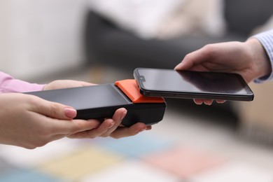 Photo of Woman paying with smartphone via terminal against blurred background, closeup