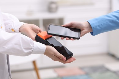 Photo of Woman paying with smartphone via terminal against blurred background, closeup