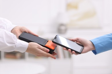 Photo of Woman paying with smartphone via terminal against blurred background, closeup