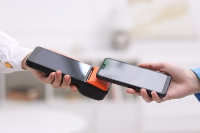 Photo of Woman paying with smartphone via terminal against blurred background, closeup