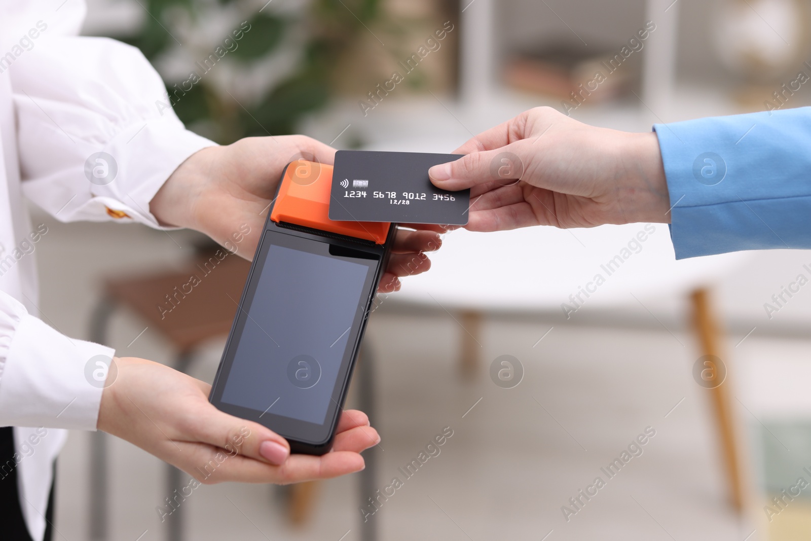 Photo of Woman paying with credit card via terminal against blurred background, closeup