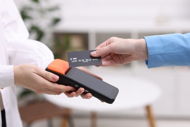 Photo of Woman paying with credit card via terminal against blurred background, closeup