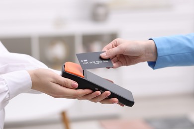 Woman paying with credit card via terminal against blurred background, closeup