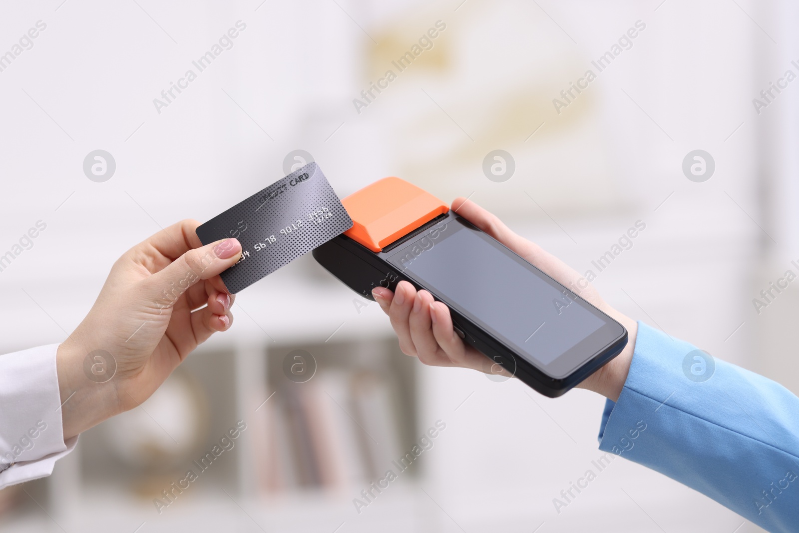 Photo of Woman paying with credit card via terminal against blurred background, closeup