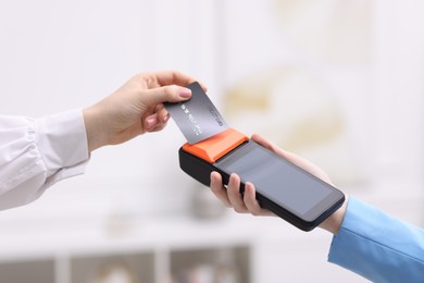 Photo of Woman paying with credit card via terminal against blurred background, closeup