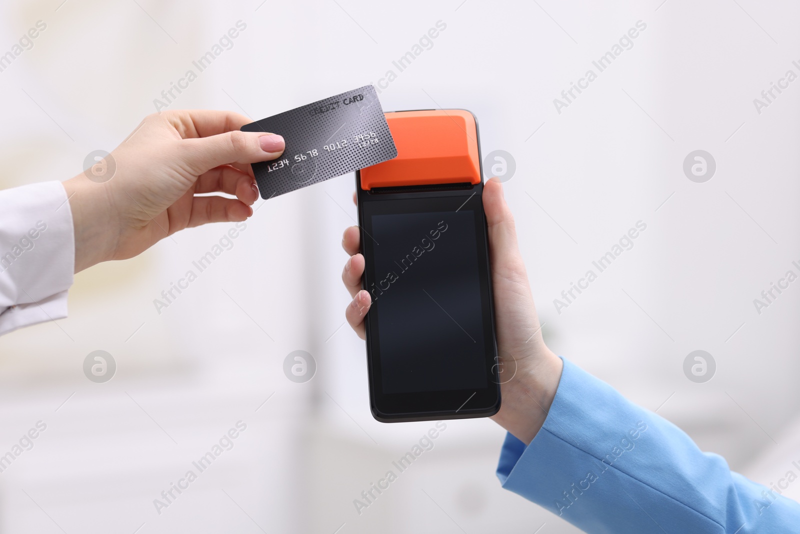 Photo of Woman paying with credit card via terminal against blurred background, closeup