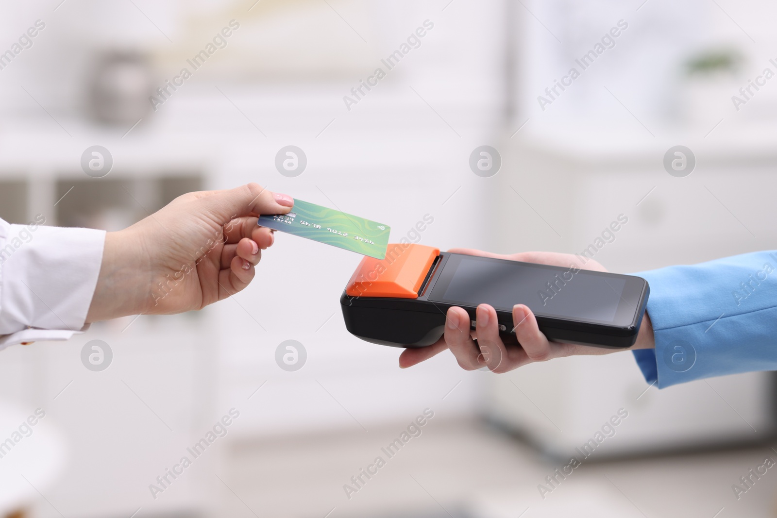 Photo of Woman paying with credit card via terminal against blurred background, closeup