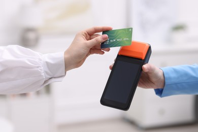 Photo of Woman paying with credit card via terminal against blurred background, closeup