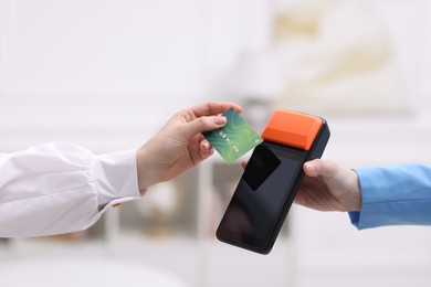 Photo of Woman paying with credit card via terminal against blurred background, closeup