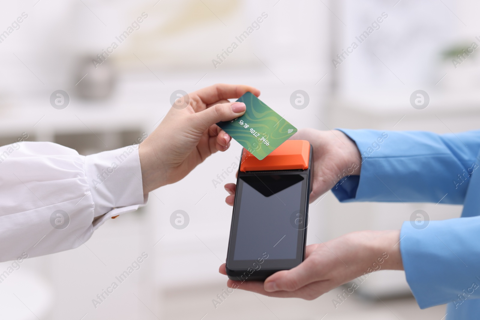 Photo of Woman paying with credit card via terminal against blurred background, closeup