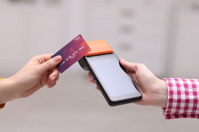 Photo of Woman paying with credit card via terminal against blurred background, closeup