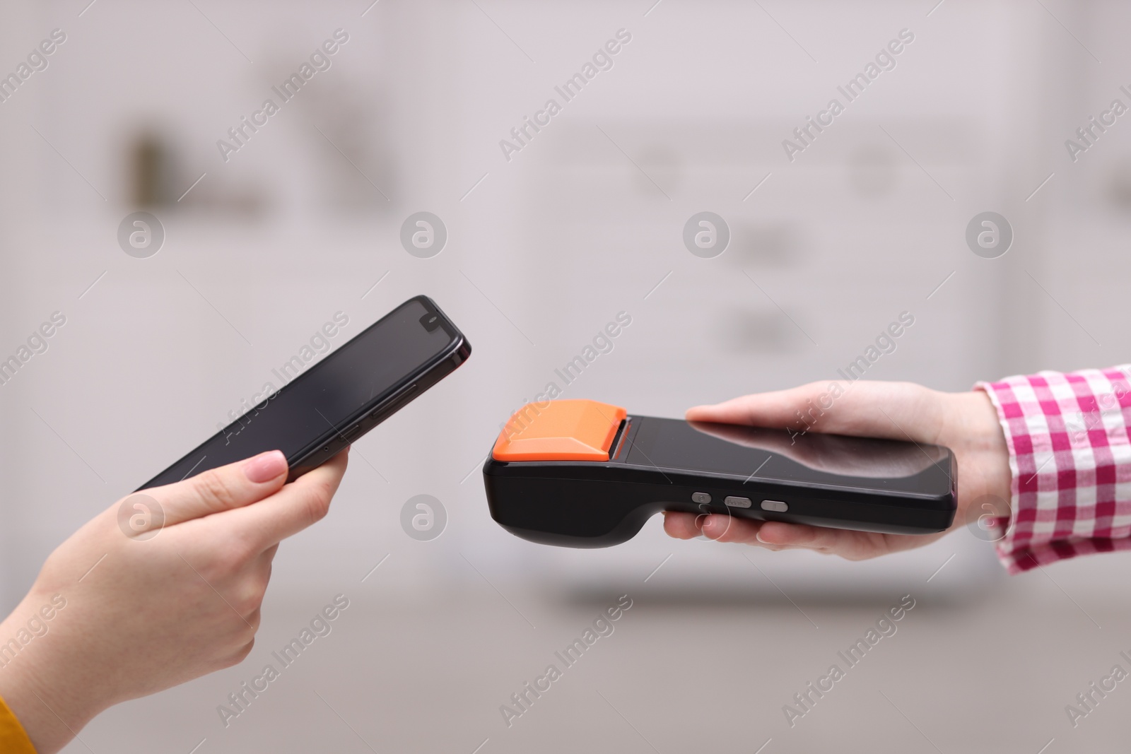 Photo of Woman paying with smartphone via terminal against blurred background, closeup