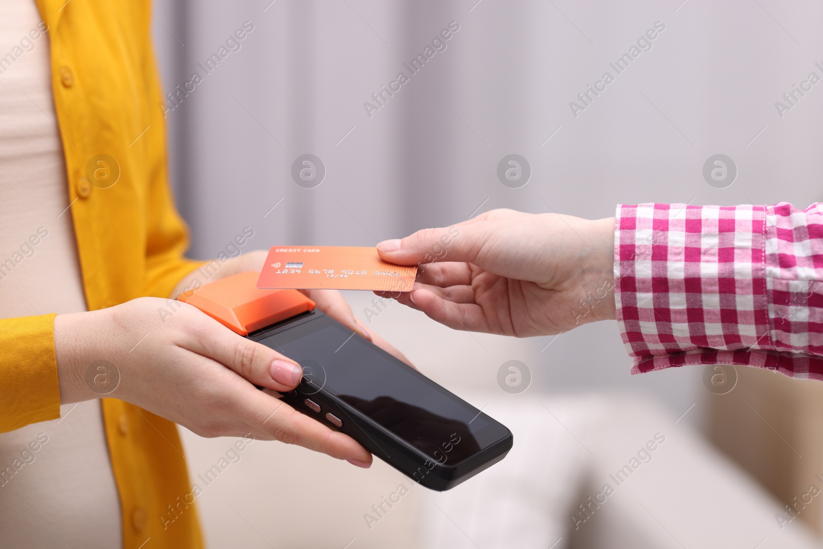 Photo of Woman paying with credit card via terminal against blurred background, closeup