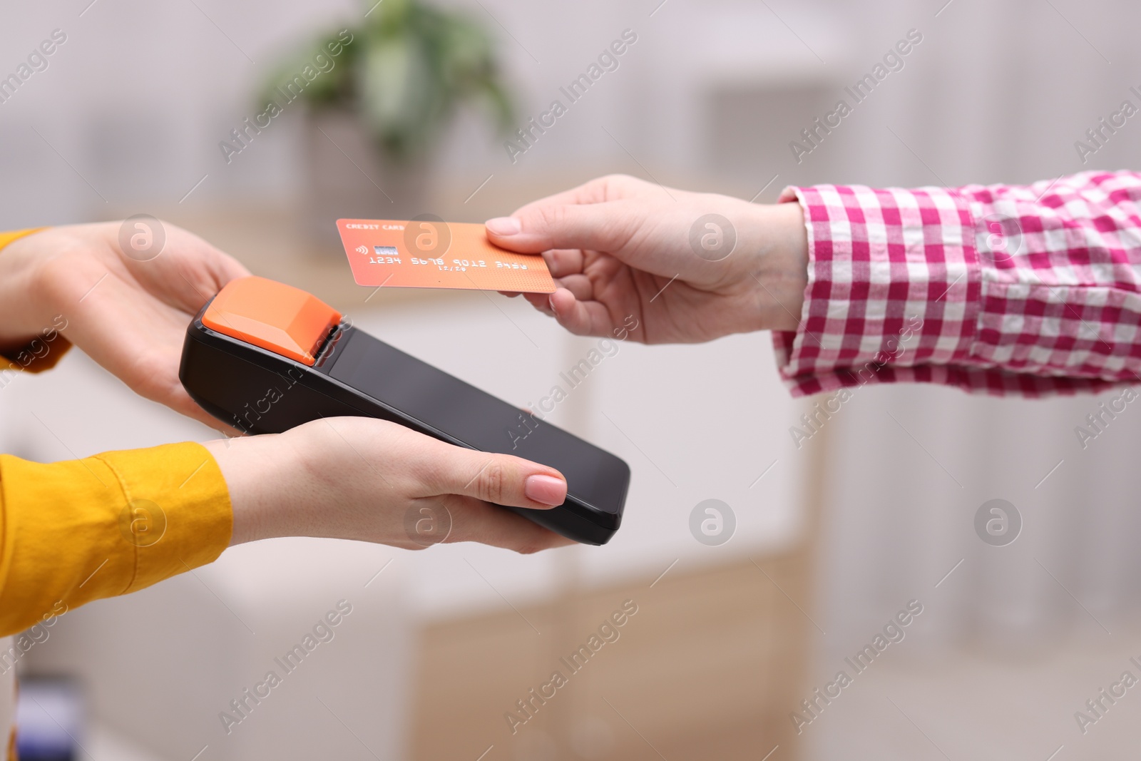 Photo of Woman paying with credit card via terminal against blurred background, closeup