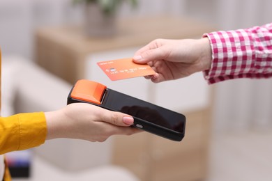 Photo of Woman paying with credit card via terminal against blurred background, closeup