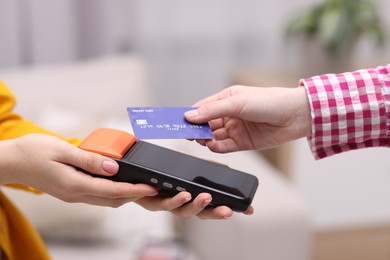 Photo of Woman paying with credit card via terminal against blurred background, closeup