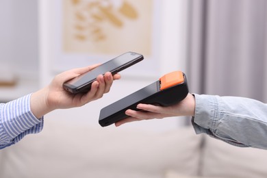 Photo of Woman paying with smartphone via terminal against blurred background, closeup