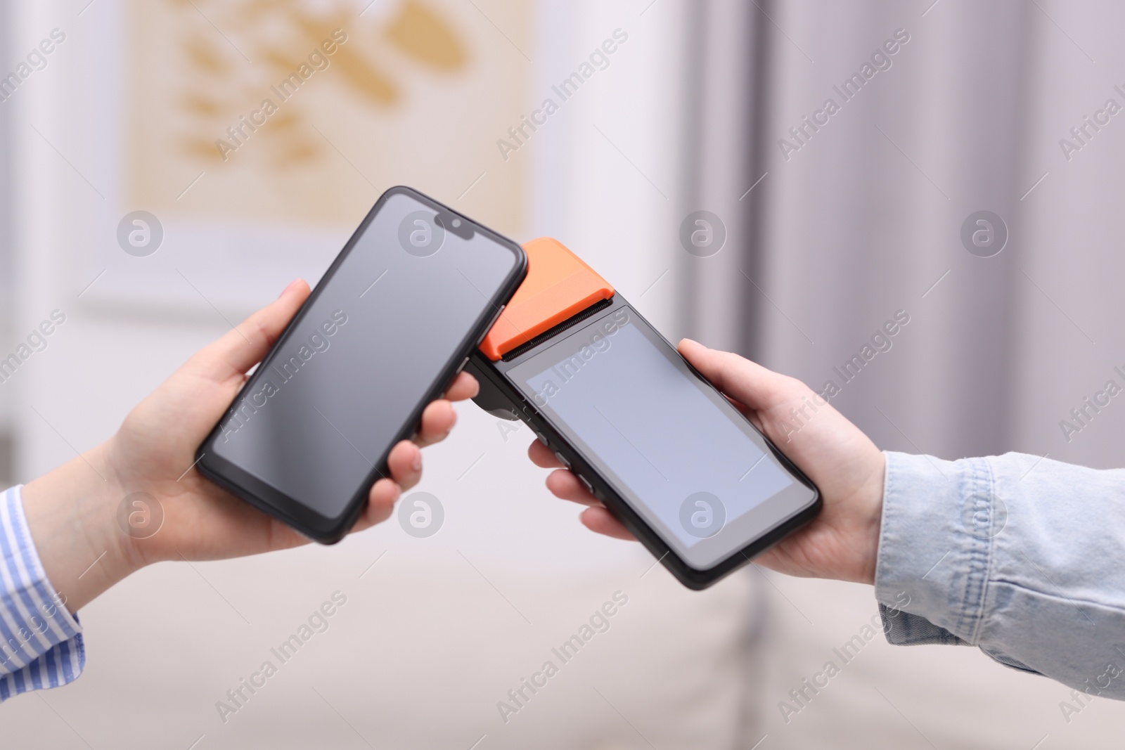 Photo of Woman paying with smartphone via terminal against blurred background, closeup