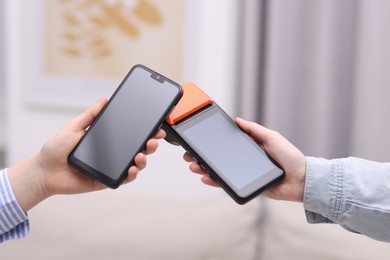 Photo of Woman paying with smartphone via terminal against blurred background, closeup