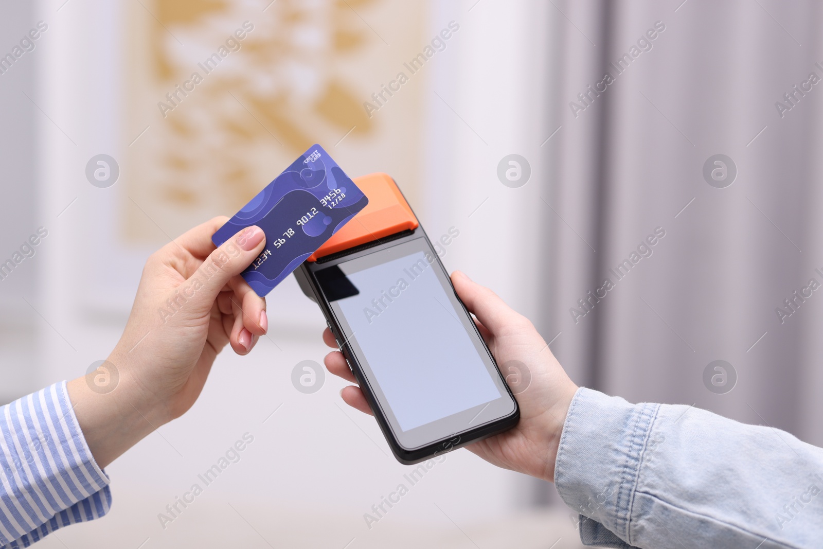 Photo of Woman paying with credit card via terminal against blurred background, closeup