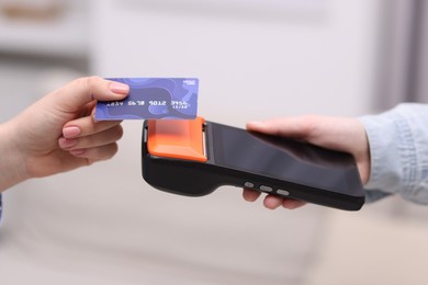 Photo of Woman paying with credit card via terminal against blurred background, closeup