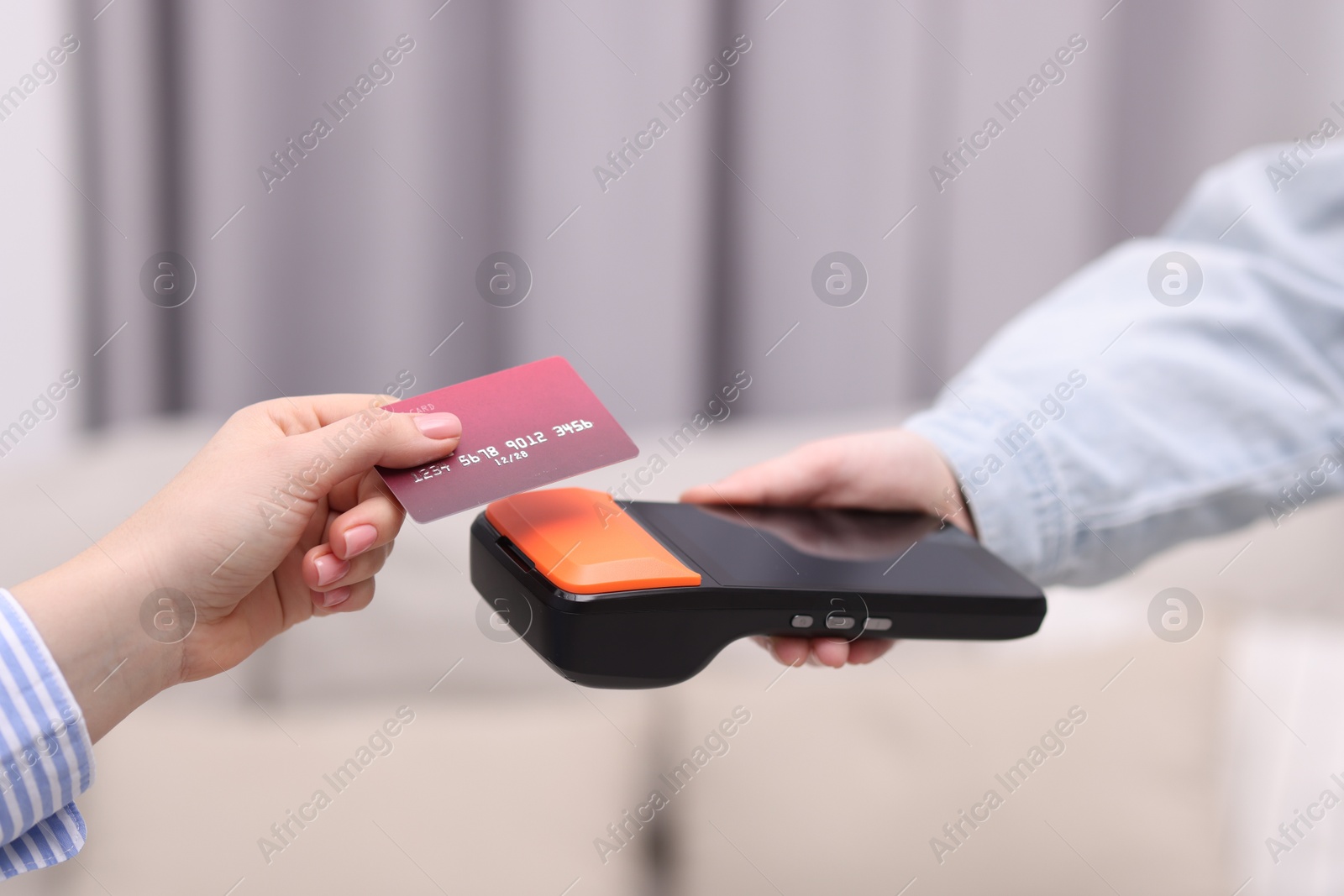 Photo of Woman paying with credit card via terminal against blurred background, closeup