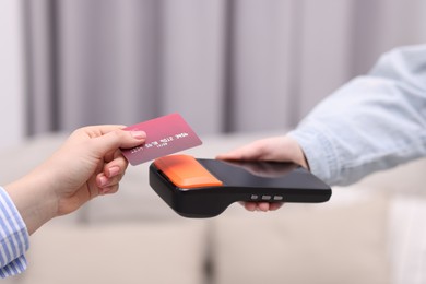 Photo of Woman paying with credit card via terminal against blurred background, closeup