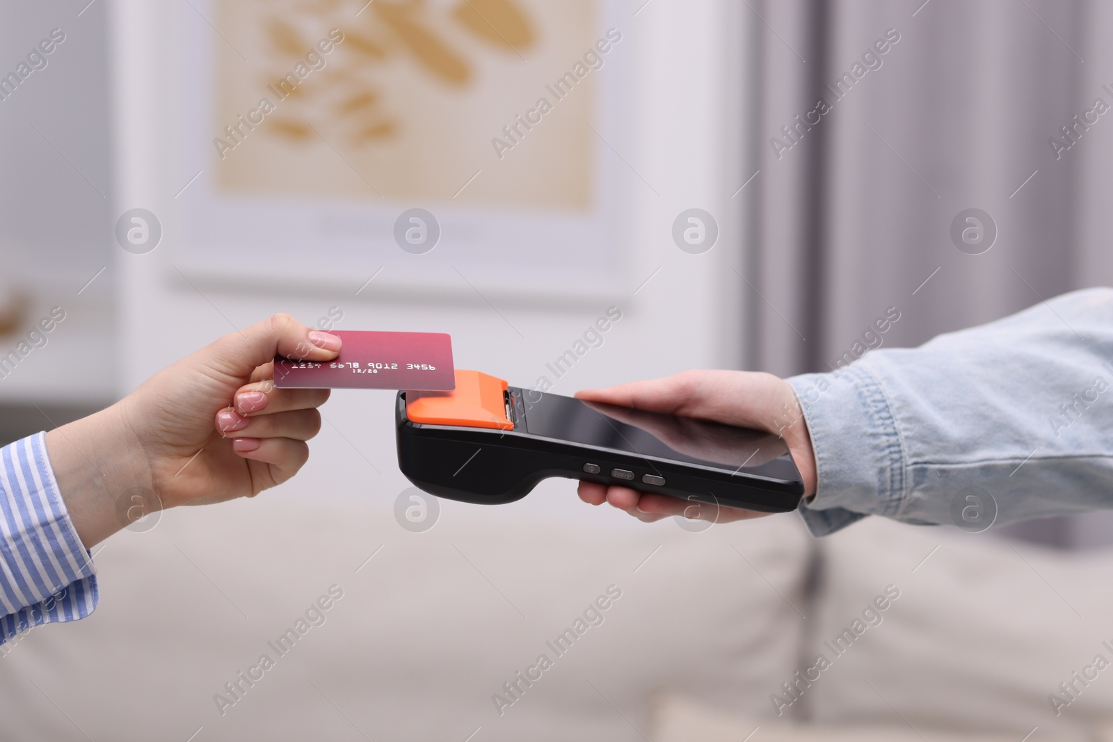 Photo of Woman paying with credit card via terminal against blurred background, closeup