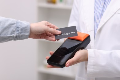 Photo of Woman paying with credit card via terminal against blurred background, closeup