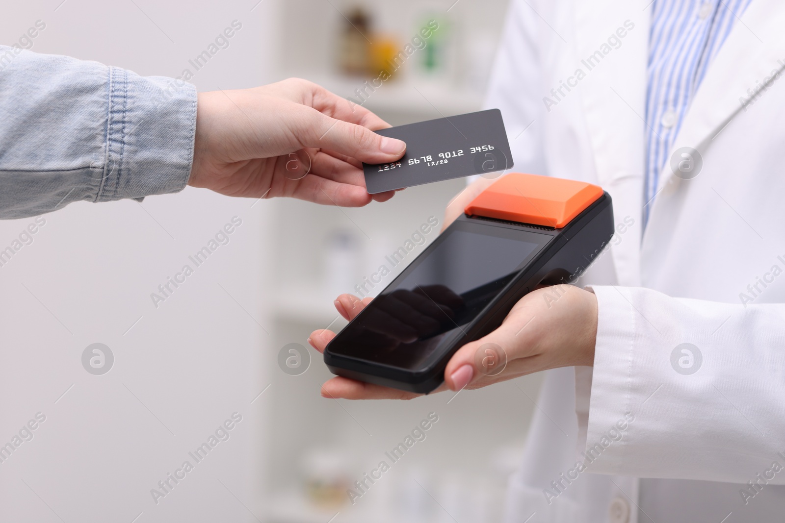 Photo of Woman paying with credit card via terminal against blurred background, closeup