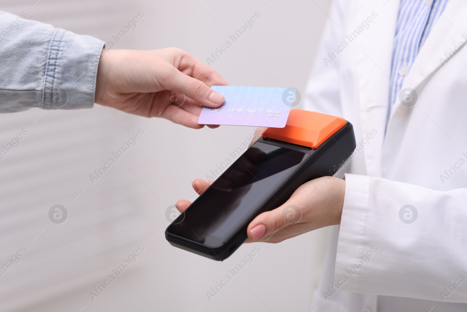 Photo of Woman paying with credit card via terminal against blurred background, closeup