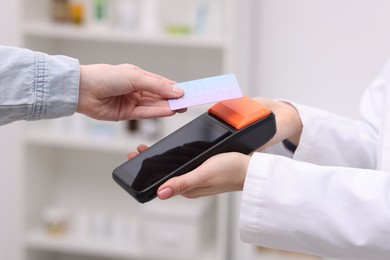 Photo of Woman paying with credit card via terminal against blurred background, closeup