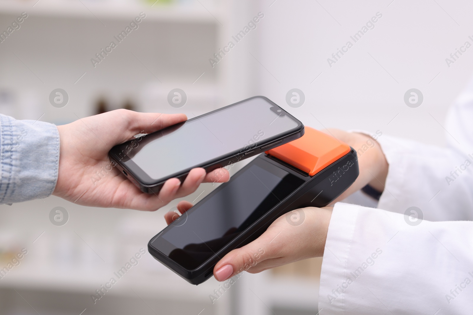 Photo of Woman paying with smartphone via terminal against blurred background, closeup