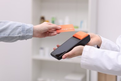 Photo of Woman paying with credit card via terminal against blurred background, closeup