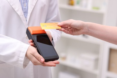 Photo of Woman paying with credit card via terminal against blurred background, closeup