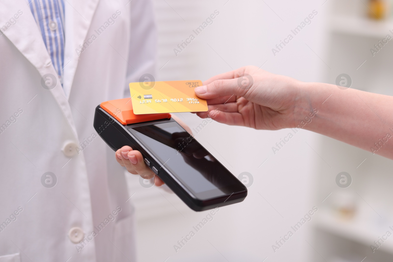 Photo of Woman paying with credit card via terminal against blurred background, closeup