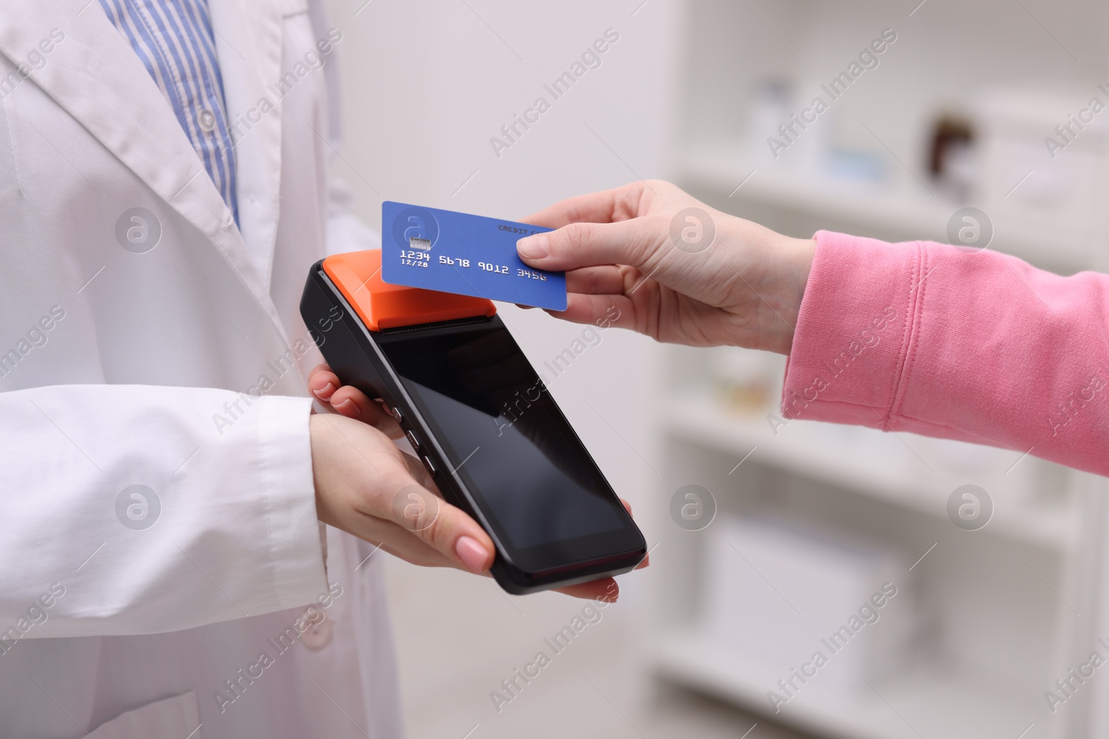 Photo of Woman paying with credit card via terminal against blurred background, closeup