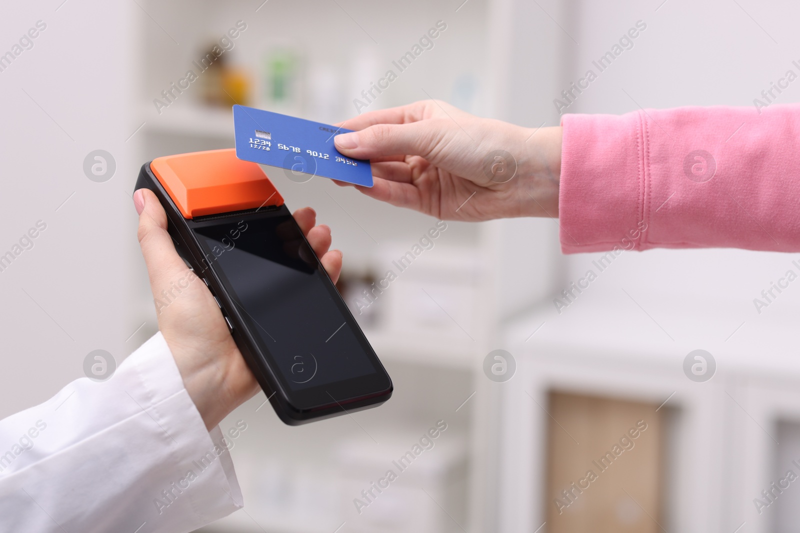 Photo of Woman paying with credit card via terminal against blurred background, closeup