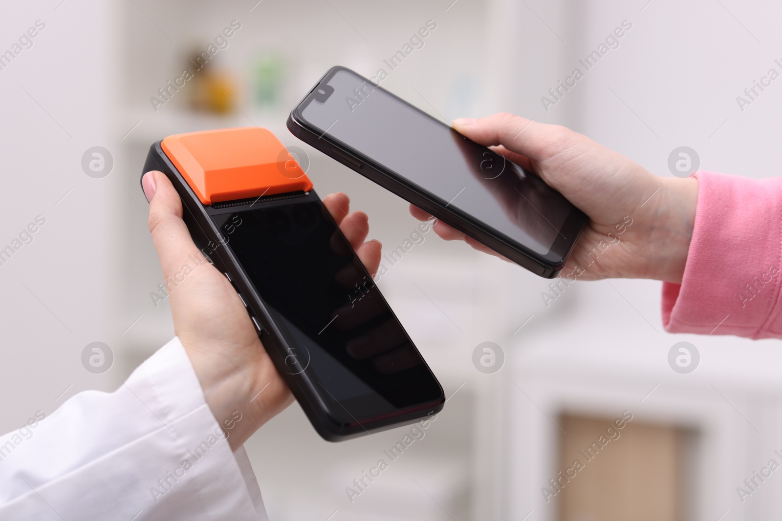 Photo of Woman paying with smartphone via terminal against blurred background, closeup