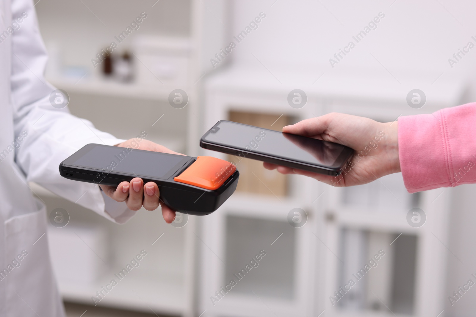 Photo of Woman paying with smartphone via terminal against blurred background, closeup