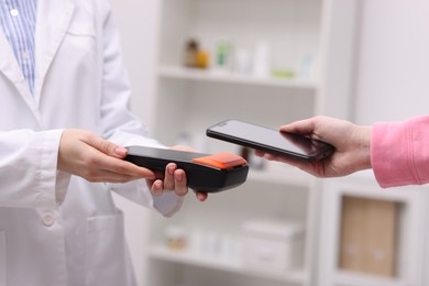 Photo of Woman paying with smartphone via terminal against blurred background, closeup