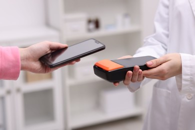 Photo of Woman paying with smartphone via terminal against blurred background, closeup