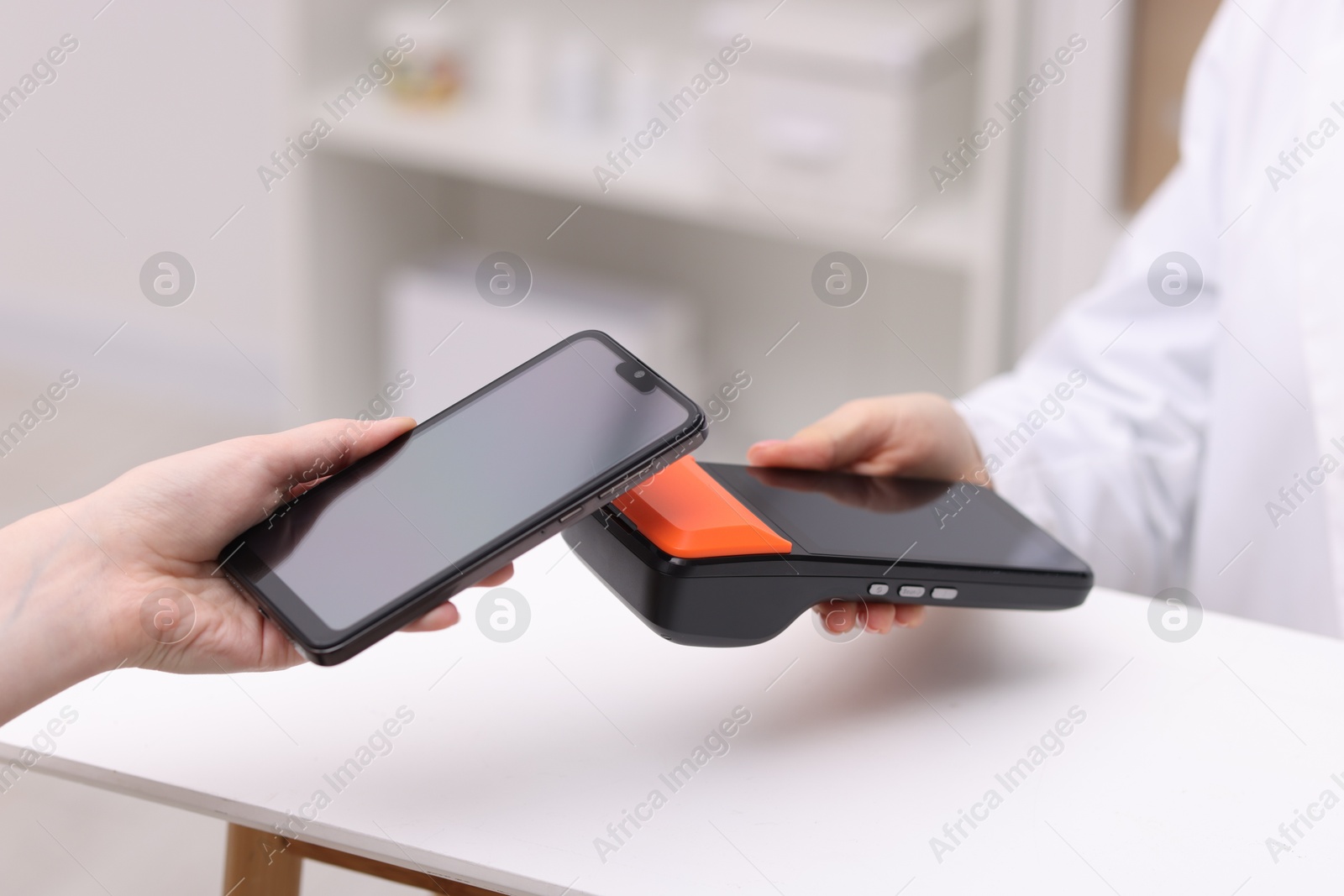 Photo of Woman paying with smartphone via terminal at counter indoors, closeup