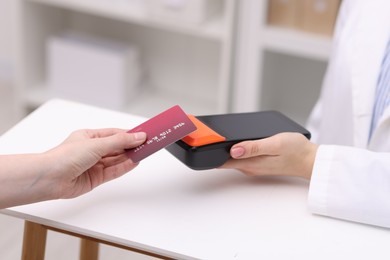 Photo of Woman paying with credit card via terminal at counter indoors, closeup